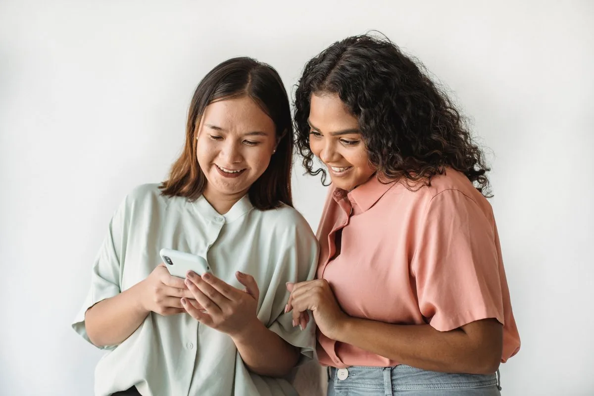 Two friends smiling at a phone together, showing real TikTok fans built by converting a bought follower boost into genuine community