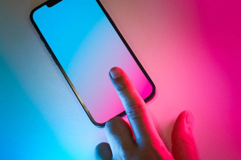 A finger tapping a glowing phone screen lit in vivid TikTok colors, the single tap of the heart that registers a like