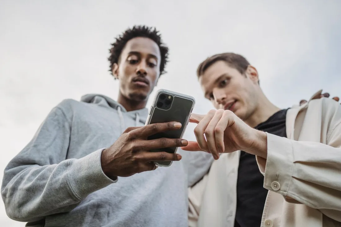 Two friends looking at one phone as one shows the other a video, the real-world moment a share creates when a video is passed from person to person