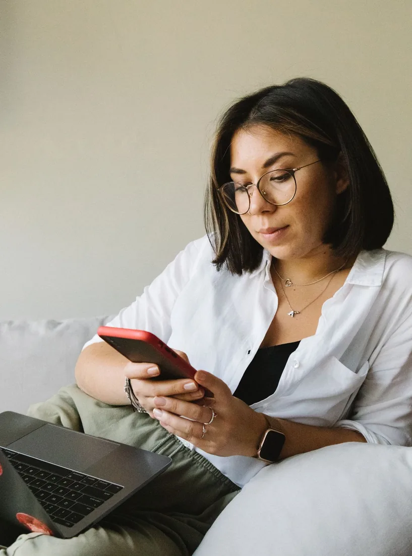 A person sitting calmly with a phone and a laptop, showing that buying shares safely means a password-free order that never puts your account at risk