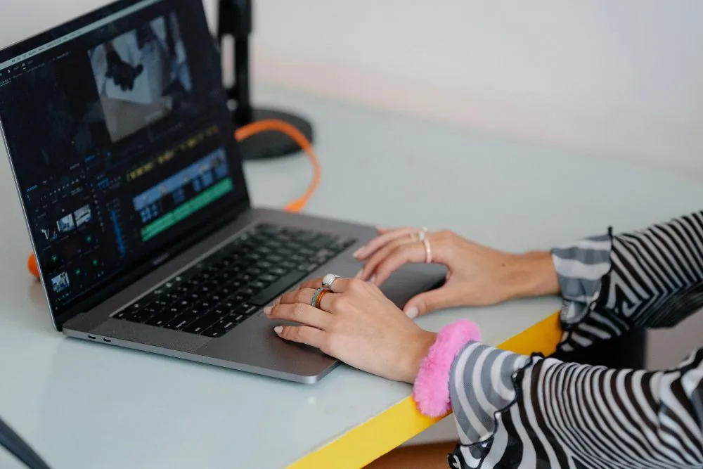 Hands editing a video on a laptop timeline, showing how to clip, title, and thumbnail a Twitch highlight so bought views convert into real reach