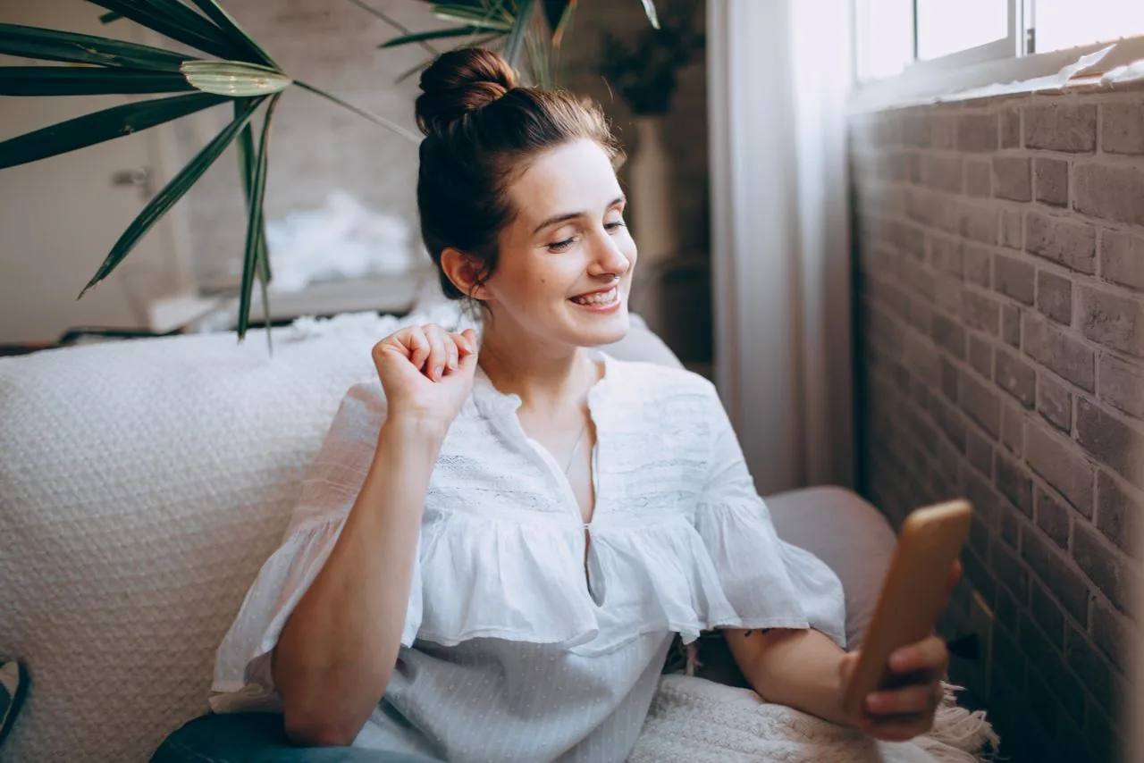 A young creator smiling as she shares a YouTube video from her phone, sending it off platform to new viewers